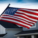 A close-up of the American flag waving in front of a suburban house, symbolizing patriotism.