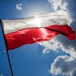 A Polish flag flutters against a bright blue sky with clouds, symbolizing national pride.