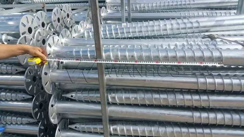 Workers and machinery installing helical screw piles for solar panels at a solar farm construction site.