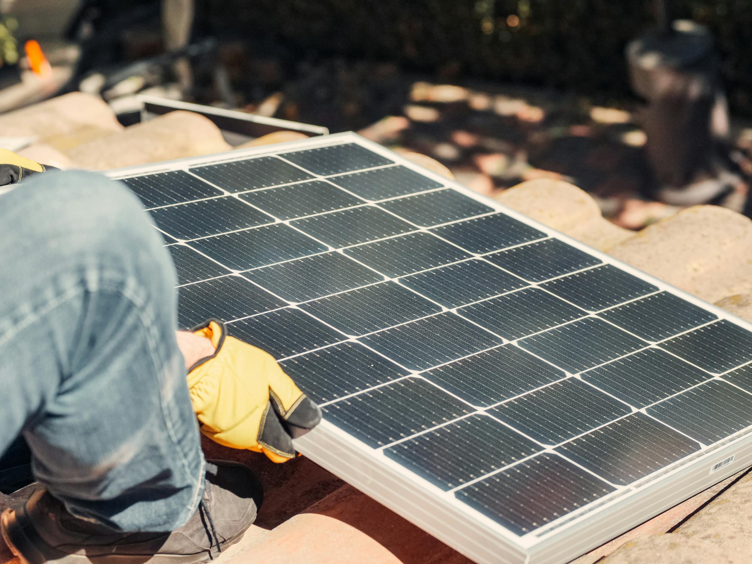 A worker installs a solar panel on a sunlit rooftop, exemplifying renewable energy